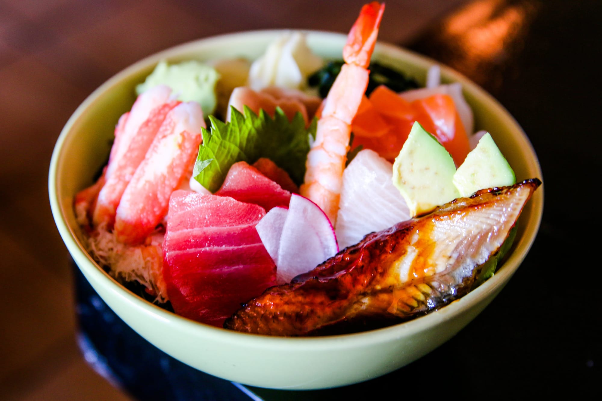 A chirashi bowl full of assorted raw fish, plus a cooked shrimp tail, a marinated fillet of eel, and slices of avocado.